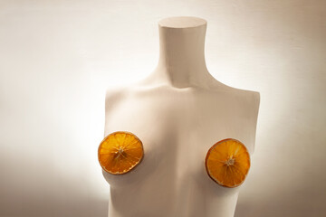 Female torso from a mannequin. Conceptual art. A minimalist female bust with orange slices on the nipples. Product advertisement for a showcase. Minimalist fashion portrait