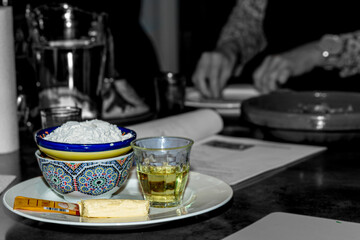 Ingredients to prepare pita bread, flour, olive oil, yeast, salt and water with a dark background, watching a book of recipes and female hands, bowls and ceramic dishes and a glass