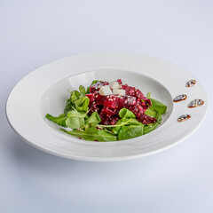 Delicious combination of arugula, beets, cheese and vinaigrette on a white ceramic plate, color, texture and flavor gathered in a salad