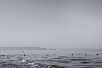 large floating sea buoys in the sea are tied with a rope. Black and white photo, border of the bathing place. vertical poster on the wall. the sea in the early morning