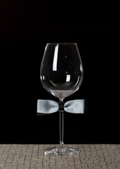 Wine glass with bow tie isolated on black background. International Bartenders Day.