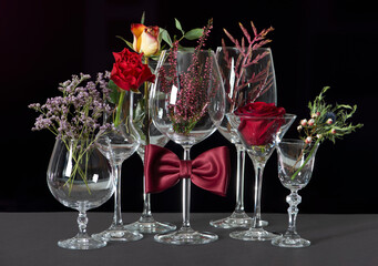 Alcohol Glasses with bow tie and flowers isolated on black background. International Bartenders Day.