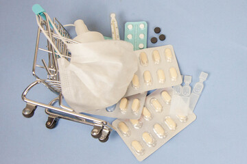Shopping cart and medicine. An expensive medicine. Cough pills shopping basket with thermometer and medicine mask on blue background.
