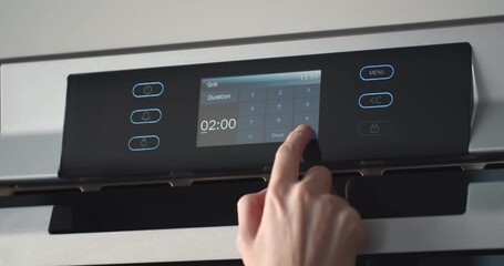 Female finger regulating temperature and time on touch panel of oven