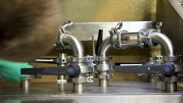 Industrial worker with protection gloves opening tank with lever. Beer flowing through tube during beer production. Close up.