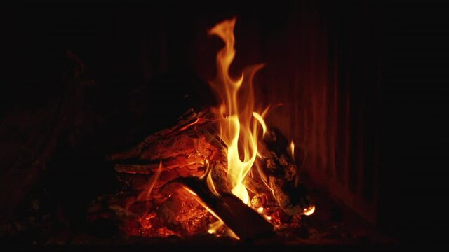Burning real wood fire with sparks jumping at a fireplace in a hotel living room in Spain. Close up of flames burning in slow motion at 120fps background footage.Concept of calm, cozy and warm place.