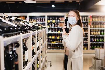 Woman in medical mask holding wine bottle in supermarket