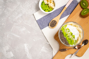 Vegan dessert with chia pudding, yogurt, banana, kiwi and seeds on concrete background with copy space. Plant based diet concept.