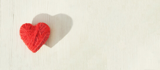 Red heart made of wool threads on a light wooden background