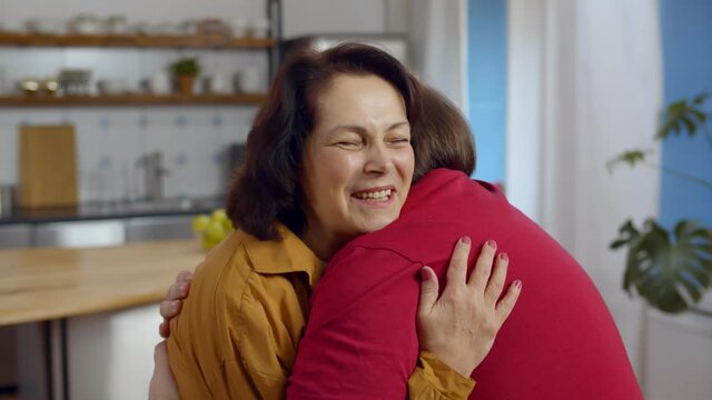 Happy smiling senior mother with adult son hugging at home