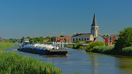 Freight ship on river Scheldt with church tower of the village of Schellebelle on a sunny day in the flemish countryside
