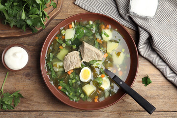 Delicious sorrel soup with meat and egg served on wooden table, flat lay
