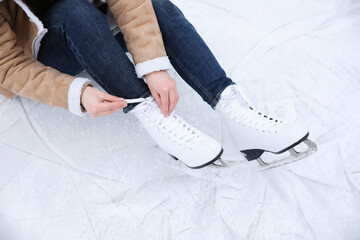 Woman lacing figure skate while sitting on ice, closeup