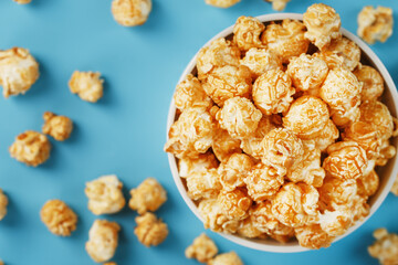 Caramel popcorn in a white glass cup with scissors on a blue background