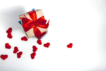 A supermarket cart filled to the brim with red hearts and a gift box wrapped in kraft paper and tied with a red ribbon on a white background. The concept of buying presents. Copy space. Top view
