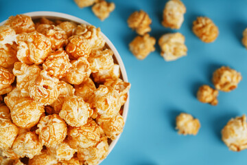 Caramel popcorn in a white glass cup with scissors on a blue background
