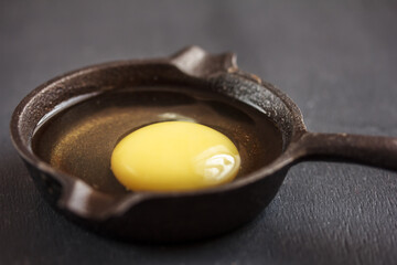 Raw organic egg in frying pan on black background. Close up. Copy space