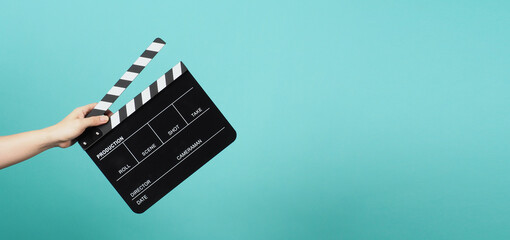 Hand is holding Black clapper board or clapperboard or movie slate on blue and green or Tiffany...