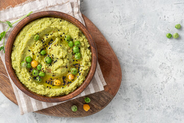 Spicy hummus of green peas and chickpeas in a wooden bowl on a grey background top view. Healthy...