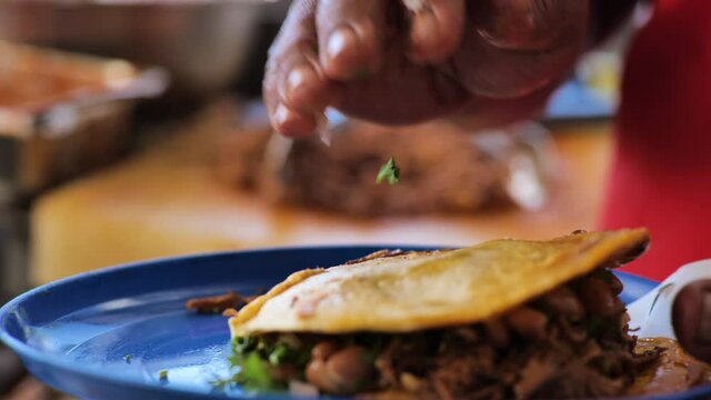 A serving of Mexican birria (stewed beef) receives a spoonful of meat juice before the tortilla is placed firmly on top, ready to be eaten.