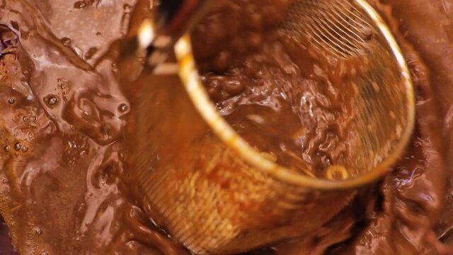 Udon noodles for ramen are tossed around in a mesh strainer inside a large pot of warm, filling, and delicious beef broth.  Close up filmed in slow motion.