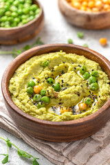 Spicy hummus of green peas and chickpeas in a wooden bowl closeup. Healthy appetizer, vegan food, vegetarian snack. Puree of green peas, chickpeas, olive oil, garlic, and cumin.