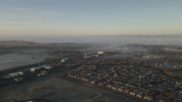 Sunrise wide angle drone footage over the Central Valley of California looking towards Sacramento and the Bay area, USA with low lying mist rolling in, pastel skies and mountains in the distance