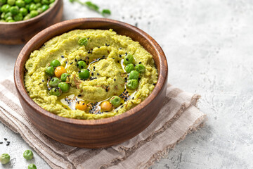 Spicy hummus of green peas and chickpeas in a wooden bowl closeup. Healthy appetizer, vegan food, vegetarian snack. Puree of green peas, chickpeas, olive oil, garlic, and cumin. Copy space for text