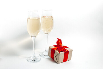 Two glasses of champagne and a gift box tied with a red ribbon on a white minimalist background. copy space