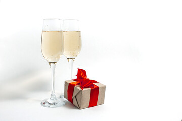 Two glasses of champagne and a gift box tied with a red ribbon on a white minimalist background. copy space