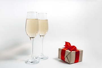 Two glasses of champagne and a gift box tied with a red ribbon on a white minimalist background. copy space