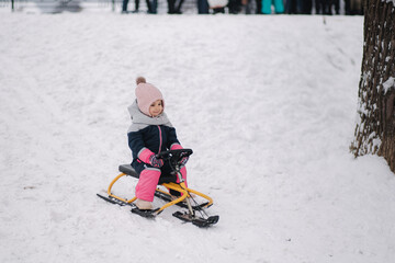 Fototapeta na wymiar Little girl enjoy a sleigh ride. Kid sledding. Kids sled in park in winter. Outdoor fun for family Christmas vacation