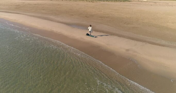 bella mujer con mascarilla covid-19 realizando posturas de yoga en la playa y vuelo dron orbital
