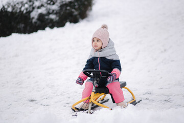 Fototapeta na wymiar Little girl enjoy a sleigh ride. Kid sledding. Kids sled in park in winter. Outdoor fun for family Christmas vacation