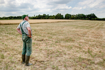 Naklejka na ściany i meble A Farmer stands on his dry meadow and hopes that the clouds in the sky will finally bring rain. Climate change is causing more and more droughts in Germany too.