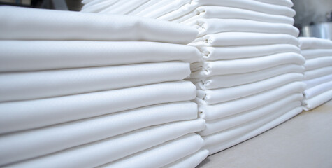 Stacks of folded white fabrics or sheets in a laundry.