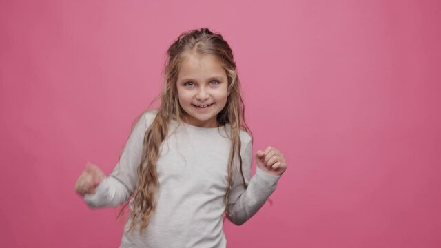 Little cute girl dancing on pink background. Happy kid listening favourite music tracks and dancing