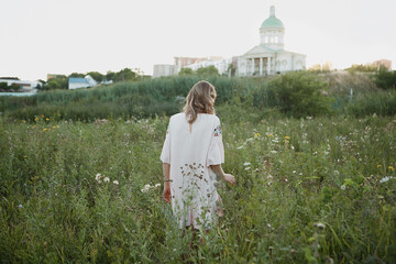 Blonde girl in pink linen dress walks in the field of flowers summer 