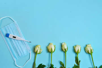 white roses, medical mask, thermometer thermometer, gifts in craft paper tied with a white satin ribbon on a bluebackground. Doctor's Day concept, flat lay top view.