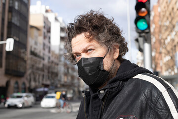 Fototapeta na wymiar portrait of blue-eyed Caucasian man with black mask for prevention of contagion next to traffic light