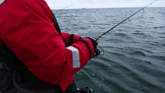 Two anglers jigging cod on a small boat out on the open sea. It is a grey, overcast winter day. The waves make the boat rock up and down.