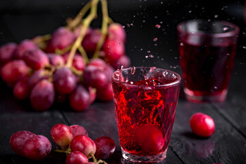A glass of fresh grape juice, grape juice canning. Dark background, splashes and drops in a glass.