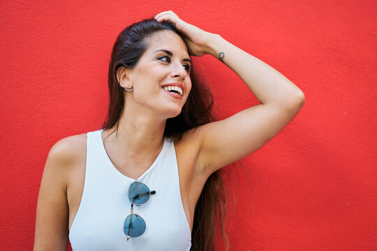 Young woman with long hair wearing stylish sunglasses and standing near red building wall in city