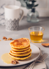 Yellow pancakes with corn flour and turmeric, dressed honey and red grapes. Healthy breakfast with superfoods. Light background, hugge scandinavian style