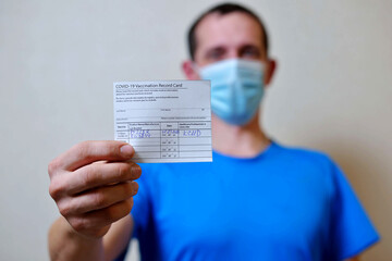 male is holding a vaccination record card and corona virus vaccine vials. Passport of immunity to...
