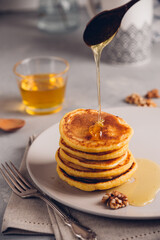 Yellow pancakes with corn flour and turmeric, dressed honey and red grapes. Healthy breakfast with superfoods. Light background, hugge scandinavian style