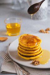 Yellow pancakes with corn flour and turmeric, dressed honey and red grapes. Healthy breakfast with superfoods. Light background, hugge scandinavian style