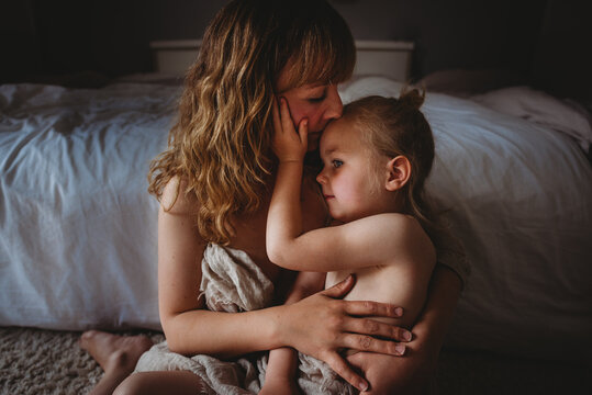 Mother kissing daughter while hugging skins to skin in bedroom