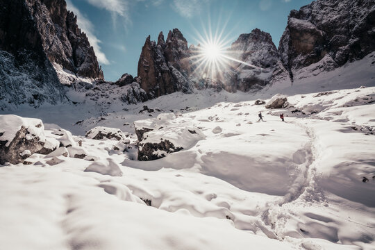 Two hikers descending in front of steep dolomite peaks under blue sky