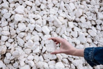 Hand holds a white chalkstone with a lot of stones on the background